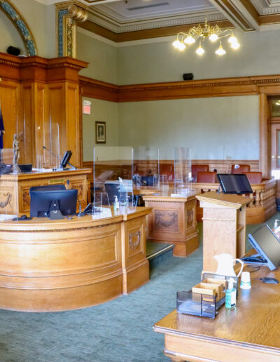 an angled photo of the judge's seat in the courtroom. the defendant and prosecution desks are visible